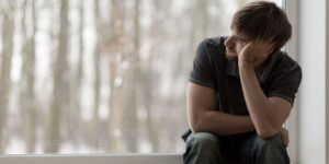 young man looking depressed sitting in window